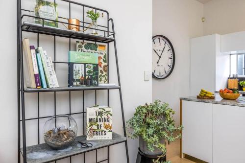 a shelf with books and plants in a room with a clock at Freemans Bay Botanical Loft - Walk to Ponsonby & Waterfront in Auckland