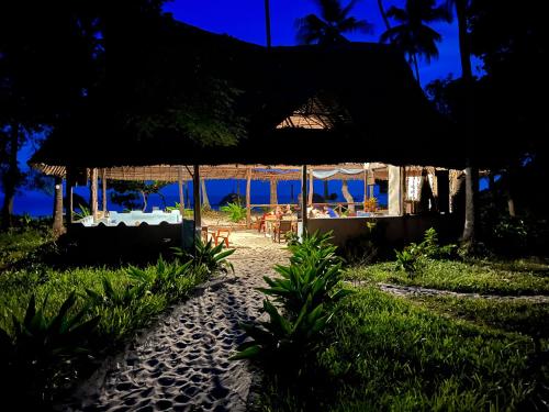 a restaurant at night with the ocean in the background at Afro Rooms & Tents in The Beach in Kilindoni