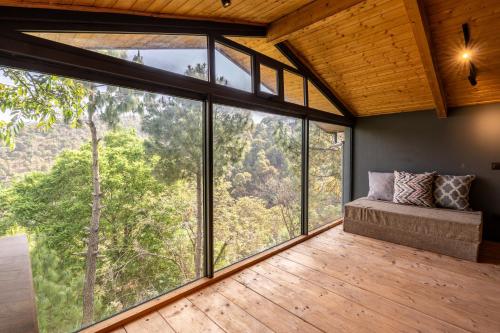 een kamer met grote ramen en een bank op een houten vloer bij SaffronStays The Hill Abode in Kasauli