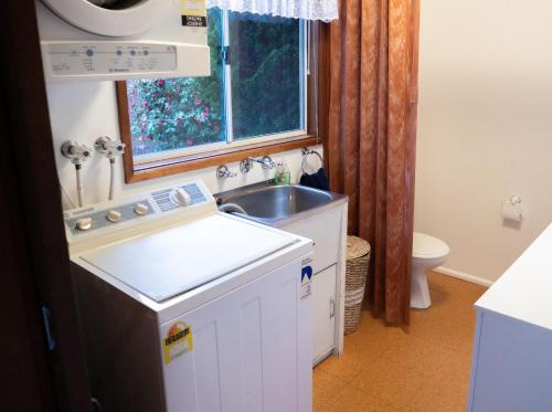 eine kleine weiße Küche mit einem Waschbecken und einem Fenster in der Unterkunft Collingwood Beach Cottage - Belle Escapes Jervis Bay in Vincentia