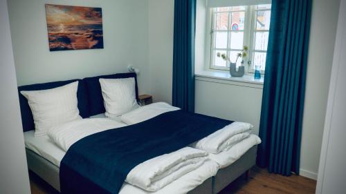 a bedroom with a bed with a blue blanket and a window at Plesners Badehotel-Lejligheder in Skagen