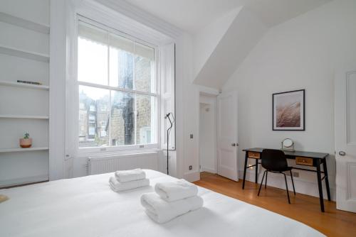 a white bedroom with a bed and a desk and a window at GuestReady - Chic in the heart of Kensington in London