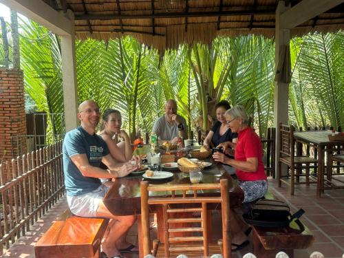 een groep mensen die rond een houten tafel zitten bij Bentre Coco Lodge in Ben Tre
