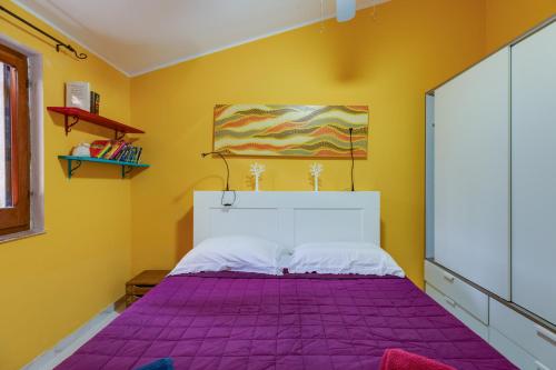um quarto com uma cama roxa numa parede amarela em Home Holidays Pintadera 1 em Bosa