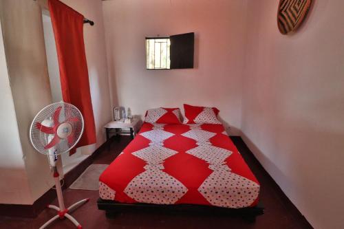 Kiriboungni chez sylfatou في Tahire: غرفة نوم بسرير احمر ومروحة