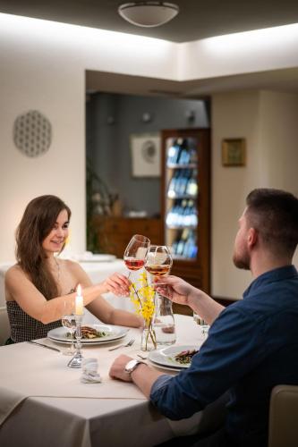 a man and woman sitting at a table with wine glasses at Hotel Radun in Luhačovice