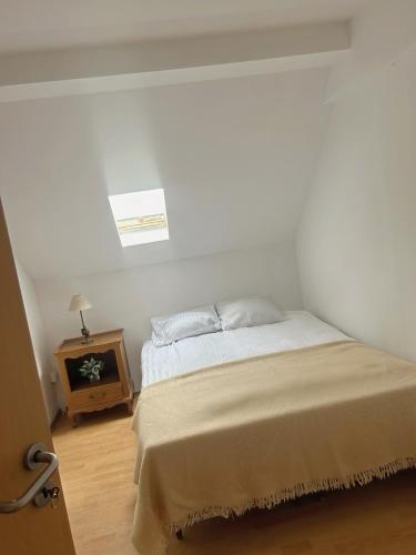 a white bedroom with a bed and a night stand at Acogedor apartamento in Dudelange