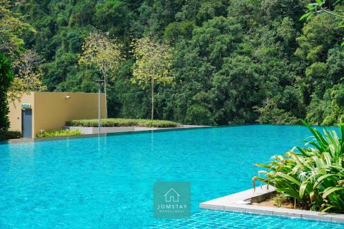 a swimming pool with blue water in front of a forest at JOMSTAY Sunway Onsen Suites Ipoh - Lost World of Tambun Ipoh Waterpark in Tambun