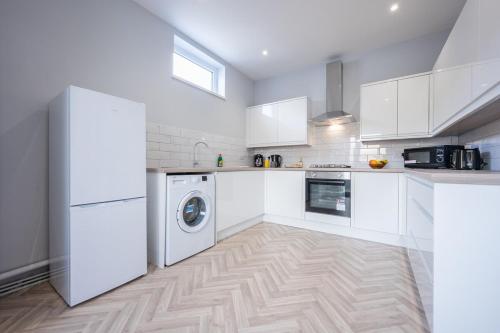cocina con armarios blancos, lavadora y secadora en Brynglas House by Tŷ SA en Newport