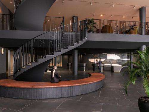 a woman sitting in a lobby with a staircase at Clarion Hotel Karlatornet in Gothenburg