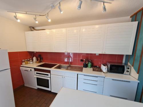 une cuisine avec des armoires blanches, un évier et un micro-ondes dans l'établissement Ref 027 A louer maison pour huit personnes jardin et accès plage, à Arzon