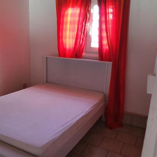 - une petite chambre avec des rideaux rouges et un lit dans l'établissement Maison créole à l'ancienne, au Lamentin