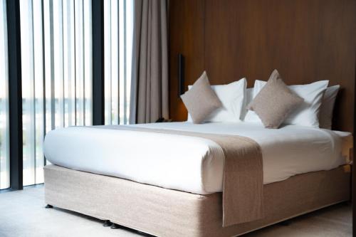 a bed with white sheets and pillows in a room with windows at ALMA Hotel Riyadh in Riyadh