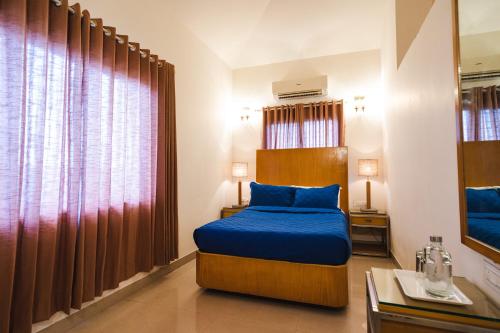 Schlafzimmer mit einem Bett mit blauer Bettwäsche und einem Fenster in der Unterkunft Villas By Hangout in Lonavla