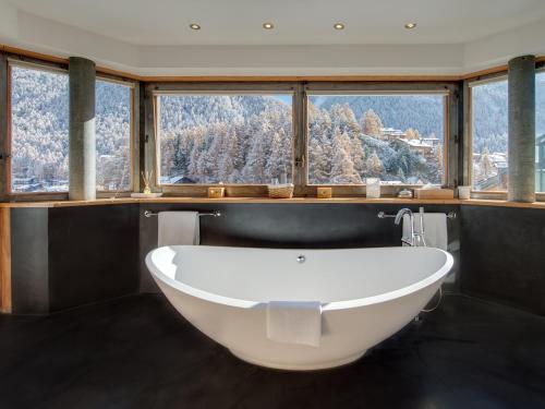 uma banheira na casa de banho com uma grande janela em Backstage Hotel Serviced Apartments em Zermatt