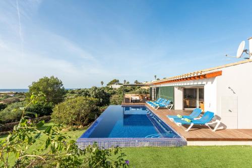 a swimming pool with two blue chairs and a house at Villa La Martina in Sant Lluis