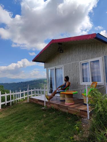 a woman sitting on the porch of a house at Adaara Retreat - Pet Friendly Cottages, Almora in Almora