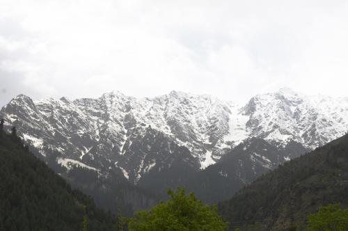 a snow covered mountain range with trees in the foreground at Manali Outdoor Retreat by Sheosante in Manāli