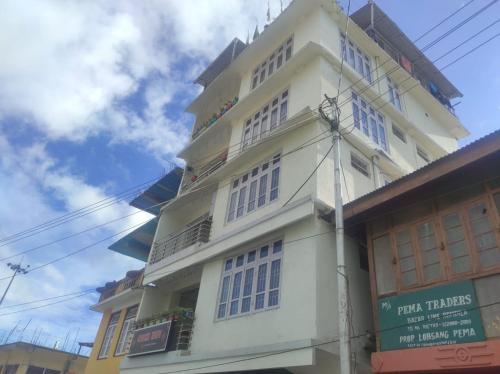 un edificio blanco alto con un cartel delante en Hotel Cozi Inn, en Bomdila