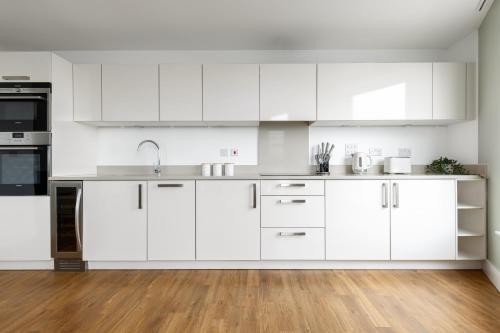 uma cozinha branca com armários brancos e piso em madeira em The Islington Collection em Londres