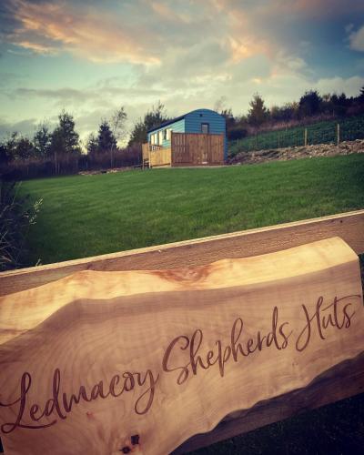 a wooden sign in front of a field with a building at Ledmacoy Shepherds Huts in Strathdon