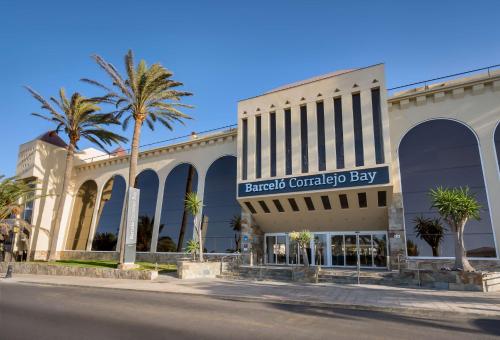 a shopping center with palm trees in front of a building at Barceló Corralejo Bay - Adults Only in Corralejo