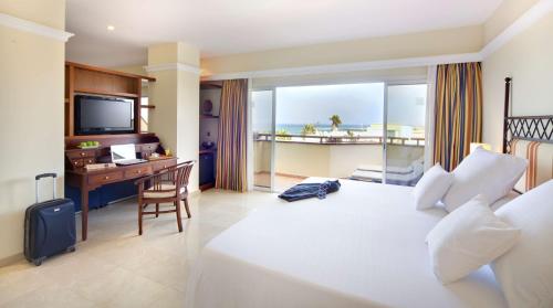 a hotel room with a bed and a desk and a television at Barceló Corralejo Bay - Adults Only in Corralejo