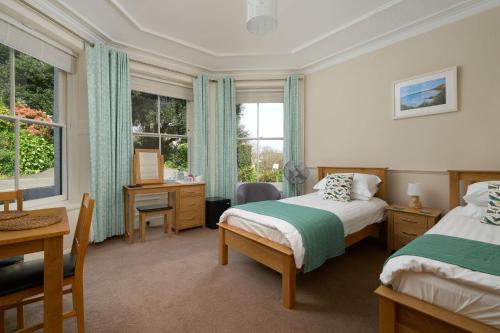 a bedroom with two beds and a desk and windows at Epchris House in Ilfracombe