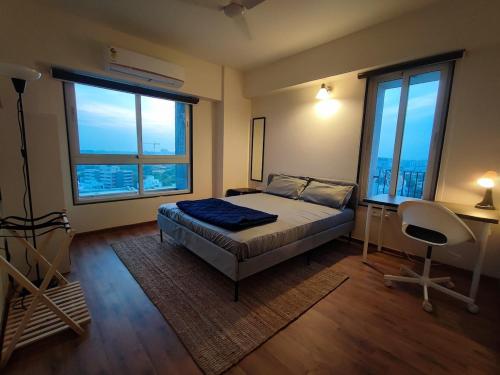 a bedroom with a bed and a desk and two windows at Alpha Room in Ahmedabad