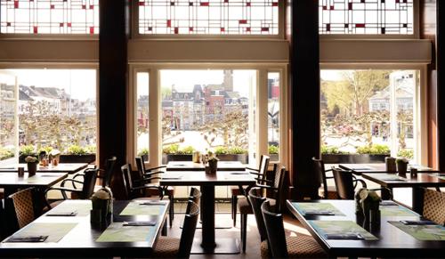 een eetkamer met tafels, stoelen en ramen bij Amrâth Hotel DuCasque in Maastricht