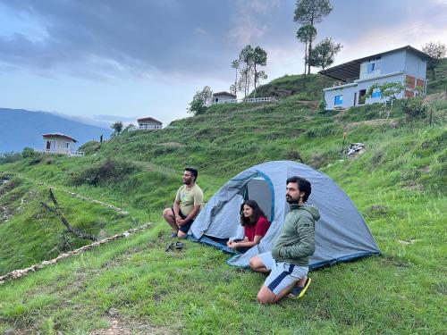 three people sitting in front of a tent on a hill at Adaara Retreat - Pet Friendly Cottages, Almora in Almora