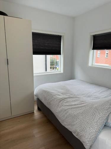 a white bedroom with a bed and two windows at Duinroos vlakbij strand in Egmond aan Zee