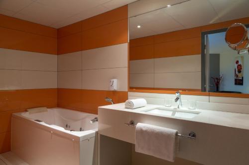 La salle de bains est pourvue d'une baignoire, d'un lavabo et d'un miroir. dans l'établissement The Originals Boutique, Actuel Hôtel, Saint-Etienne Aéroport, à Andrézieux-Bouthéon