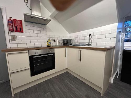 una cocina con armarios blancos y horno negro en Rock Park Penthouse, en Llandrindod Wells