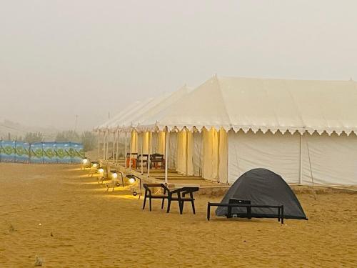 a row of tents with tables and benches in the sand at Venture Desert Camp Jaisalmer in Jaisalmer