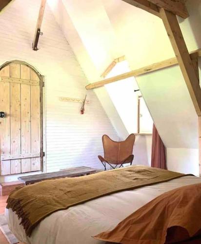 une chambre avec un lit et une chaise dans un grenier dans l'établissement Chaumière normande et sa dépendance, proche Deauville et Honfleur 10-12 pers, à Quetteville