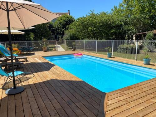 a swimming pool with an umbrella next to a wooden deck at Le Logis du Canal in Marennes
