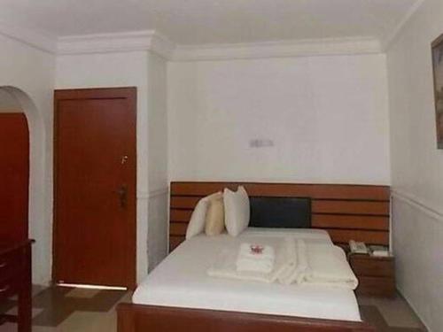 a bedroom with a white bed with a wooden headboard at Precious Palm Royal Hotel in Benin City