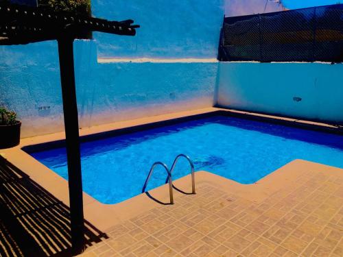a swimming pool with an umbrella next to a blue wall at Hotel nuevo atardecer in Cabo San Lucas