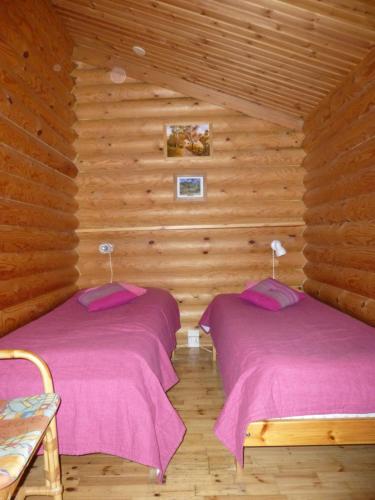 two beds in a room with wooden walls at Cottages SAA in Punkaharju