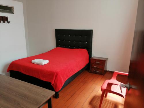 a bedroom with a bed with a red blanket and a table at Hotel El Carretero in Popayan
