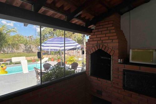 a brick fireplace with a view of a patio and an umbrella at Casa Sossego com Piscina em Chapada dos Guimarães in Chapada dos Guimarães