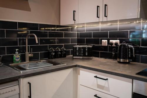 a kitchen with white cabinets and a sink and black tiles at Turkish Baths Retreat, City Centre in Sheffield