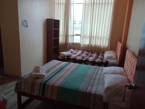 a small room with two beds and a window at Hostal El Conde in Tacna