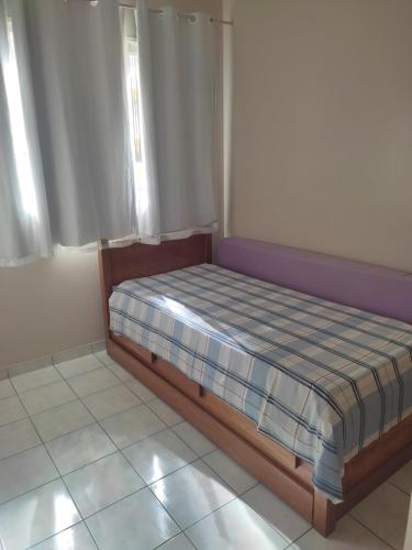 uma pequena cama num quarto com duas janelas em Claudia Apartment em Vila Velha