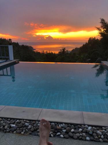 a person laying on the edge of a swimming pool at sunset at Luxurious Pool villa with great sea view in Ko Phangan