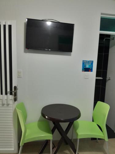 聖安德烈斯的住宿－Brisas del Mar Apto 1B，一张桌子和两张绿色椅子,墙上有一台电视机