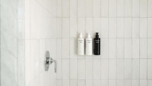 a white tiled bathroom with two bottles on the wall at Longfellow Hotel in Portland