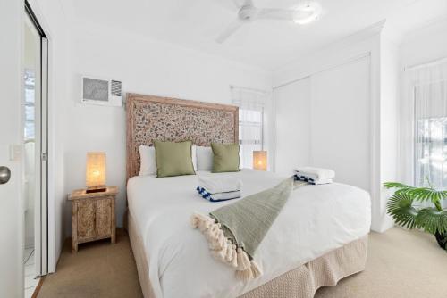 a white bedroom with a large white bed with green pillows at Oasis - Pool, Wifi & Free Parking in Cairns