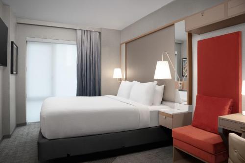 ニューヨークにあるSpringHill Suites by Marriott New York Manhattan Times Squareの白いベッドと赤い椅子が備わるホテルルームです。